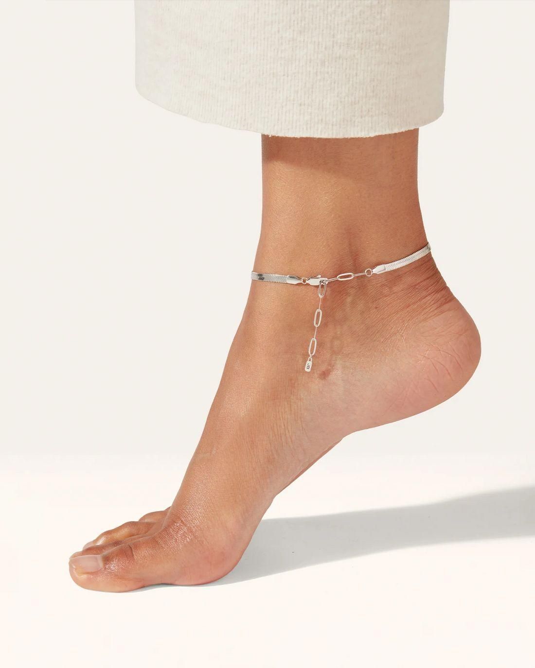 Silver anklet on a foot with a plain background
